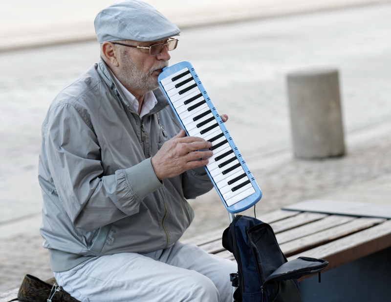 20 - An older man playing a blue melodica, a free-reed wind instrument with a small keyboard on top